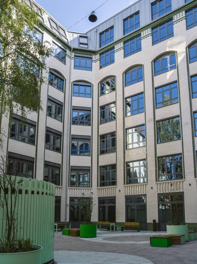 Inner courtyard of a multi-storey building with white façades, many windows and green seating areas